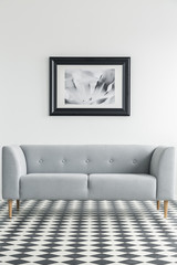 Simple, grey sofa on a checkered floor with a painting in the backgorund in a living room interior. Real photo