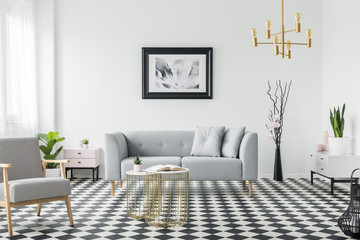 Real photo of a modern living room interior with a grey sofa, armchair, painting, golden lamp and...