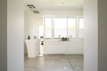Fototapeta na wymiar Mirror on white cabinet next to washbasin in bright bathroom interior. Real photo