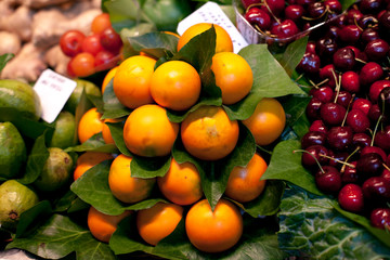 Fresh,oranges and cherries in greenery at a local farmers market in Barcelona Spain. Counter with heap of berries.