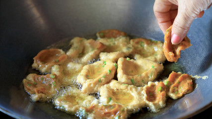 Fried fish cakes or patty, in the pans background with hot oil and woman hands, Thai foods concept.