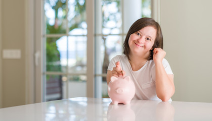 Down syndrome woman at home holding piggy bank screaming proud and celebrating victory and success...