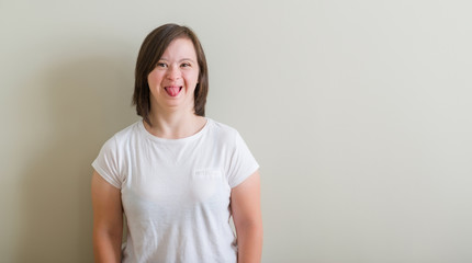 Obraz premium Down syndrome woman standing over wall sticking tongue out happy with funny expression. Emotion concept.