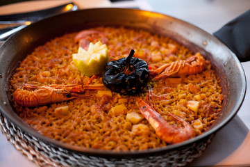 close-up of delicious seafood valencia paella with king prawns, rice with spices and lemon wedges...