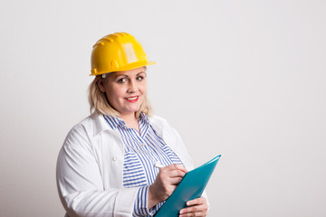 Portrait of an attractive overweight woman with yellow helmet in a studio.
