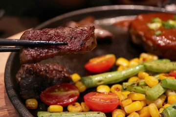 Premium quality Beef Steak slices in set with black chopsticks, medium rare grilled, and some vegetable in the plate as foods background, Japanese style. Warm dark tone.