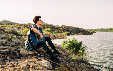 Naklejka na ściany i meble young man plays guitar on nature near lake