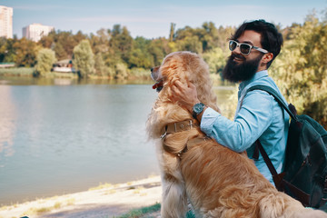 Young man sitting with his dog on the chair in the park, enjoyin