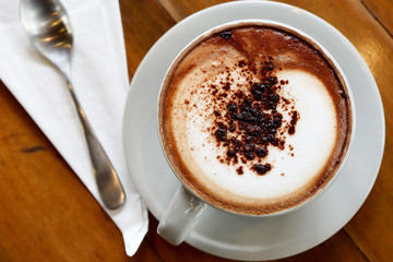 Hot Mocha Fresh Coffee in a white cup with milk foam art on the wooden table background. Drink concept.