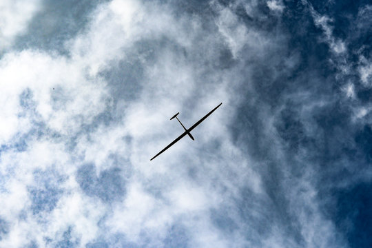 A glider flying high on a blue cloudy sky.
