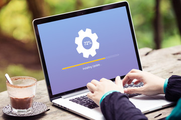 Woman working and Installing update process with gearbox percentage progress and loading bar on laptop / computer at the park / outdoor