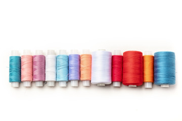 An overhead photo of a row of thread spools, shot from above on a white background with copy space