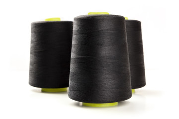 A side view of large black thread spools on a white background with copy space