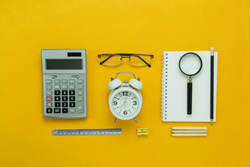 Table top view aerial image of back to school of education season background concept.Flat lay accessories for business finance the clock & calculator and objects on modern rustic yellow paper.