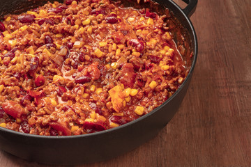 A large cast iron pan with chili con carne, on a dark background with copy space