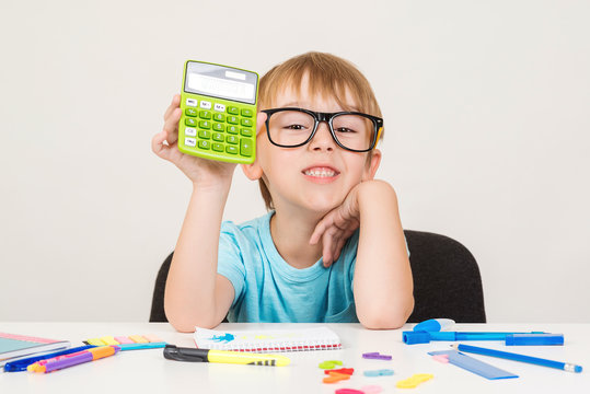 Smart boy using calculator. Kid in glasses figuring out math problem. Developing logical skills. Happy school boy doing homework. Smart kid in glasses at table with school supplies. Back to school. - Powered by Adobe