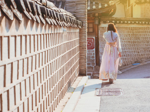 travel and tourist asia concept from backside long hair woman in korea traditional cloth (hanbok) walk in vintage town and old brick wall with soft focus background