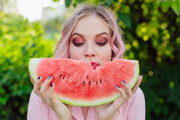 Beautiful young woman with pink hair enjoying watermelon