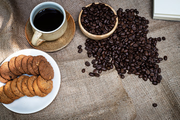 The ceramic coffee cup put at the middle of dish of cookies and coffee beans,on hemp cloth