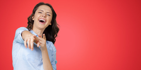 Young woman laughing and pointing on you isolated on pink background