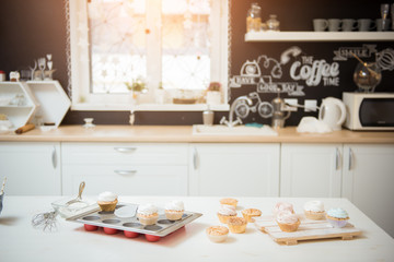 Preparation of brown cupcakes with white cream on the table of modern kitchen