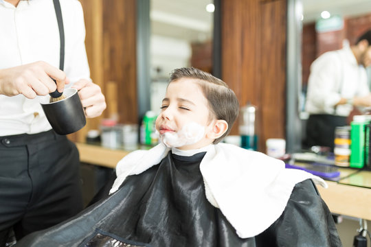 Barber Applying Shaving Foam On Boy's Face In Shop