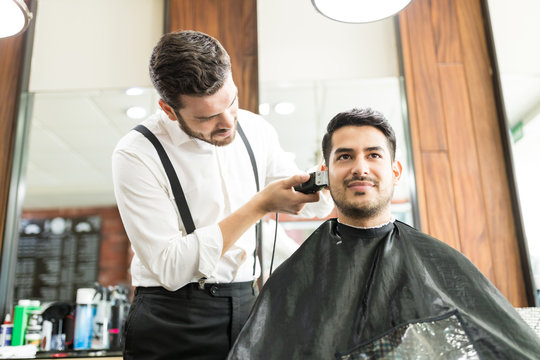 Customer Smiling While Barber Trimming His Hair In Shop