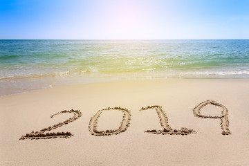 Year 2019 written at the sand beach with sea wave water
