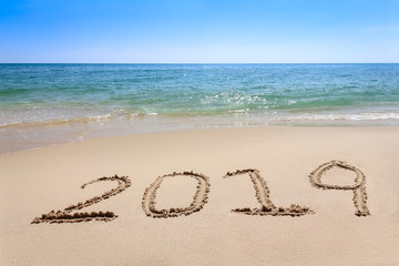 Year 2019 written at the sand beach with sea wave water