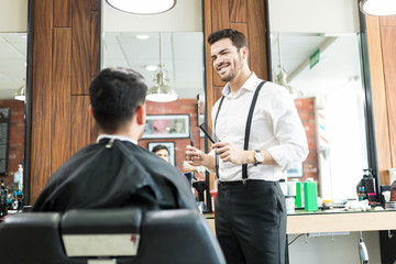 Smiling Male Hairstylist Looking At Client In Barber Shop