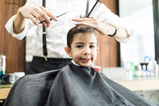 Boy Smiling While Getting Haircut By Barber In Salon