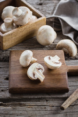 Fresh Raw Mushrooms Champignons on a Wooden Cutting Board on Old Rustic Wooden Table Background