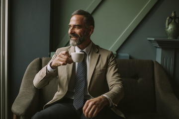 Handsome senior businessman drinking coffee in lobby