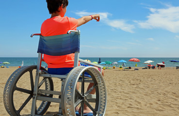 boy on a special wheelchair indicates the horizon of the sea on