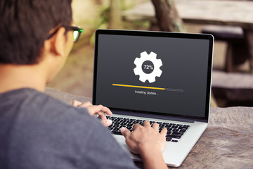 Man working and Installing update process with gearbox percentage progress and loading bar on laptop / computer at the park / outdoor - 216685921