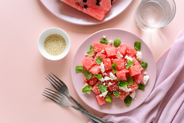Summer watermelon salad with feta cheese, sesame seeds and mint leaves on pink plate. Healthy eating concept