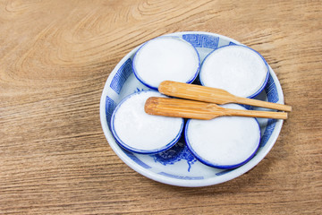 Thai Coconut Milk Custard is a thai dessert made from rice flour, coconut milk and sugar put the small ceramic cups place are on a wooden floor. Khanom Thuai,