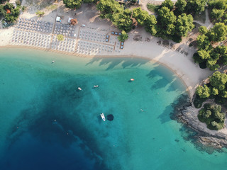 Aerial view of bright turqoise water and beach with pine forest.