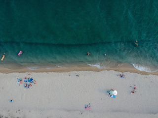 Aerial view of bright turqoise water and beach with a few people.