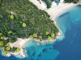 Aerial view of bright turqoise water and beach with pine forest.