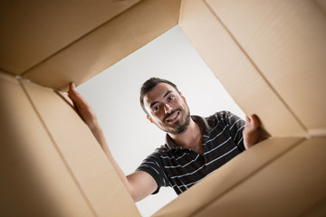 Man smiling, unpacking, opening carton box and looking inside. The package, delivery, surprise,...
