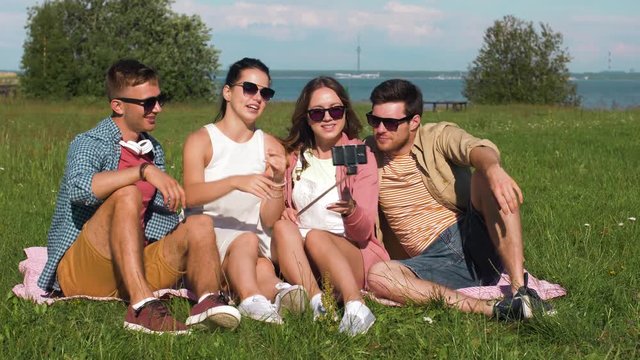 friendship, leisure and technology concept - group of happy smiling friends taking picture by selfie stick outdoors at summer park in tallinn, estonia