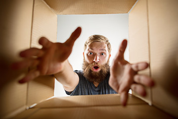 The surprised man unpacking, opening carton box and looking inside. The package, delivery, surprise, gift lifestyle concept. Human emotions and facial expressions concepts