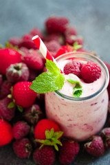 Pink berry smoothie or milk shake in glass jar with fresh raspberry and strawberry background, top view