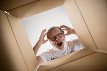 The surprised senior man unpacking, opening carton box and looking inside. The package, delivery, surprise, gift lifestyle concept. Human emotions and facial expressions concepts