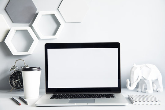 Modern and design workspace with laptop mock up screen, office accessories , elephant figures and cup of coffee. Gray interior with hanging hexagone shapes. Design space for freelancer.