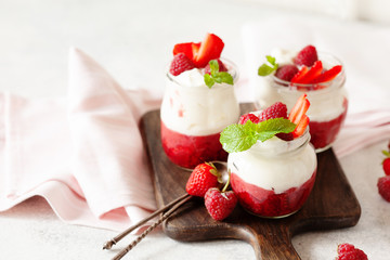 Jars of natural white yogurt with berry sauce decorated with fresh strawbeery, raspberry and mint