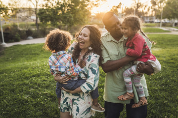 Cheerful parents carrying children on field at park during sunset