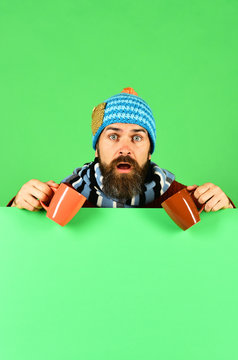Man in warm hat holds brown cups on green background
