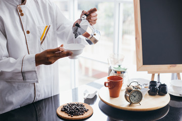 Young barista pouring coffee into a cup at cafe restaurant with happiness